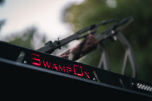 Load image into Gallery viewer, Closeup from below of red backlit Swamp Ox logo on roof rack.
