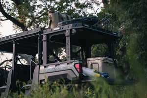 Lower side view of UTV featuring Swamp Ox roof and bed rack in outdoor setting during the day. Black textured powder-coated hood rack carrying outdoor gear and duck hunting equipment. Includes light package, unlit.