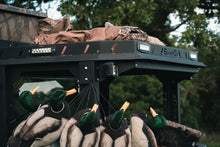 Load image into Gallery viewer, Upper closeup side view of UTV featuring Swamp Ox bed and roof racks in outdoor setting during the day. Black textured powder-coated hood rack carrying outdoor gear and duck hunting equipment. Includes light package, unlit.
