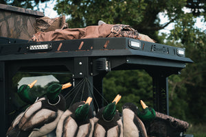 Upper closeup side view of UTV featuring Swamp Ox bed and roof racks in outdoor setting during the day. Black textured powder-coated hood rack carrying outdoor gear and duck hunting equipment. Includes light package, unlit.
